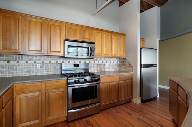 kitchen with dark wood-type flooring, tasteful backsplash, appliances with stainless steel finishes, and a towering ceiling