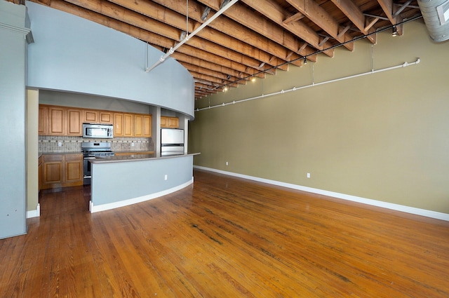 kitchen with tasteful backsplash, stainless steel appliances, dark hardwood / wood-style floors, a center island, and a towering ceiling