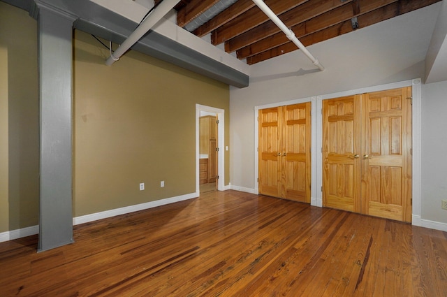 unfurnished bedroom featuring hardwood / wood-style floors, multiple closets, and beam ceiling