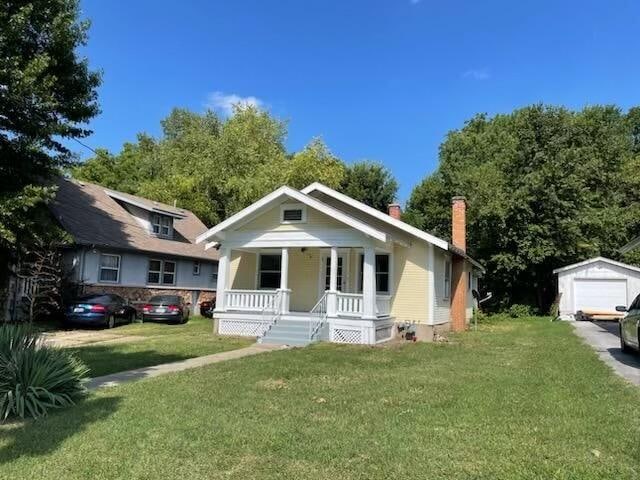 bungalow featuring a garage, an outbuilding, a front lawn, and covered porch