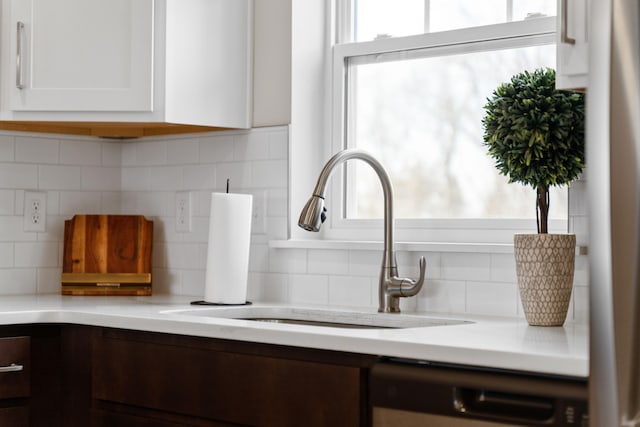 interior details with dishwashing machine, sink, tasteful backsplash, and white cabinetry