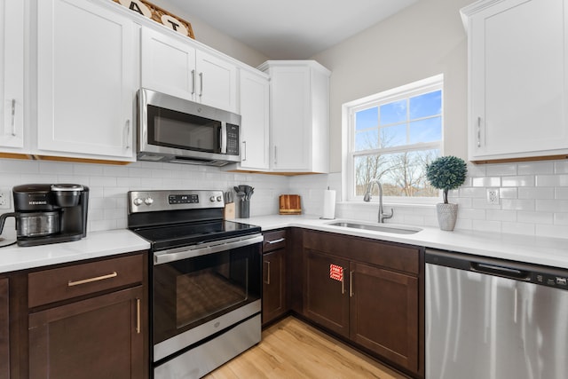 kitchen with white cabinets, stainless steel appliances, light wood-type flooring, and sink