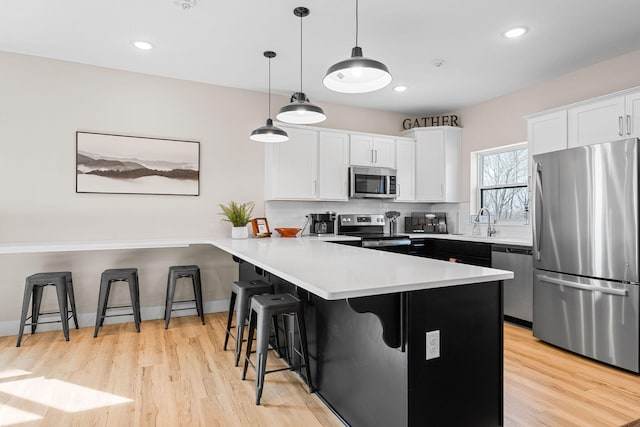 kitchen with a breakfast bar area, stainless steel appliances, kitchen peninsula, hanging light fixtures, and white cabinetry