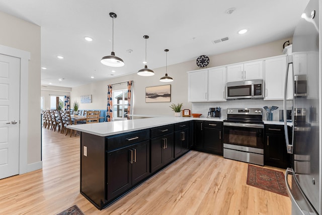 kitchen with decorative light fixtures, stainless steel appliances, kitchen peninsula, and white cabinets