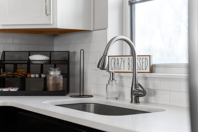 room details with tasteful backsplash, light stone countertops, sink, and white cabinets