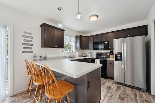 kitchen with pendant lighting, a breakfast bar area, light hardwood / wood-style flooring, kitchen peninsula, and black appliances