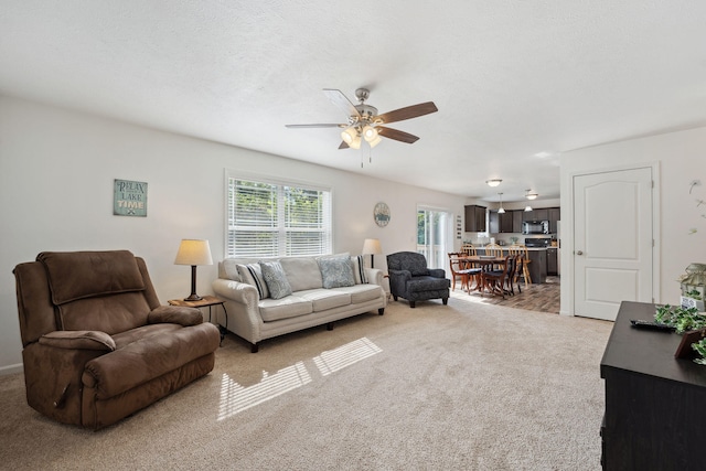 living room with ceiling fan, a textured ceiling, and light carpet