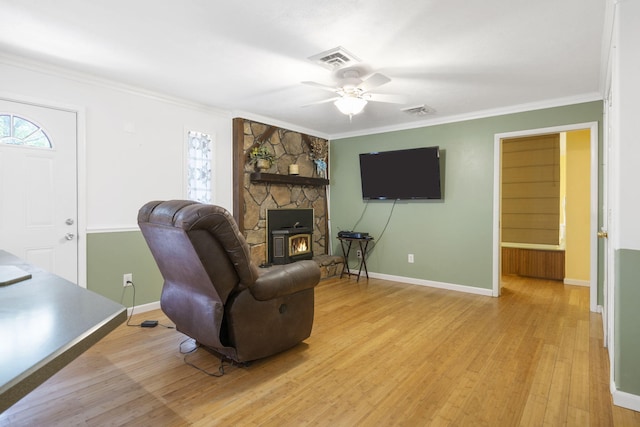 living room with a wood stove, ornamental molding, light wood-type flooring, and ceiling fan