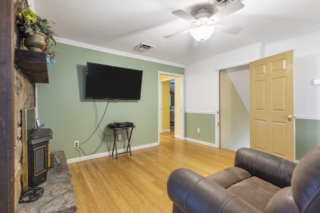 living area with visible vents, wood finished floors, ceiling fan, a wood stove, and ornamental molding