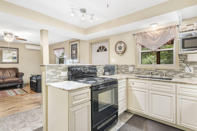 kitchen with a wall mounted air conditioner, a sink, a peninsula, tasteful backsplash, and black electric range oven