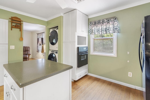 kitchen with white cabinets, light hardwood / wood-style flooring, stacked washer / dryer, black appliances, and crown molding