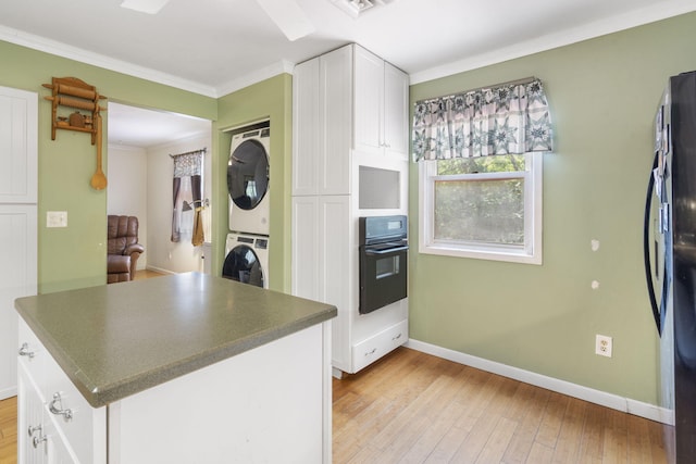 kitchen featuring stacked washer / dryer, dark countertops, black appliances, light wood-style flooring, and white cabinetry
