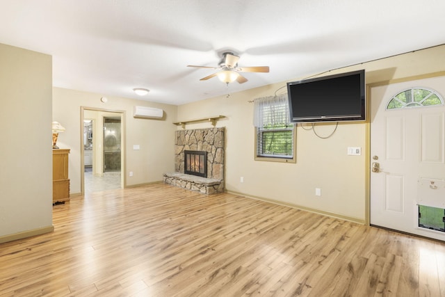 unfurnished living room featuring a ceiling fan, light wood-type flooring, baseboards, a fireplace, and a wall mounted AC