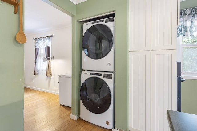 washroom with light wood-style floors, baseboards, stacked washing maching and dryer, and laundry area