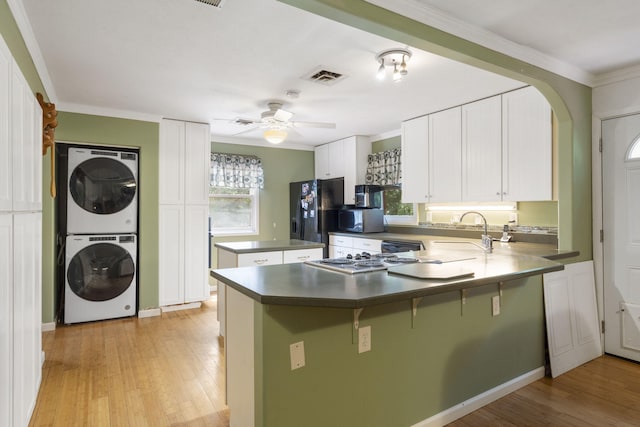 kitchen featuring stacked washer and dryer, light hardwood / wood-style floors, kitchen peninsula, white cabinetry, and appliances with stainless steel finishes