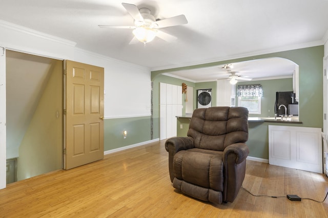 living area with crown molding, arched walkways, a ceiling fan, and light wood-style floors
