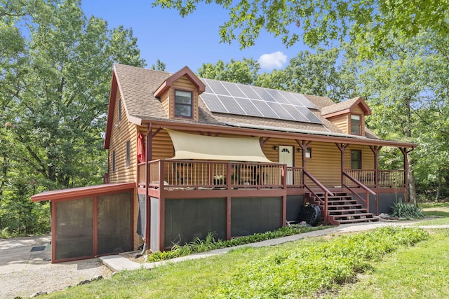 rustic home featuring a shingled roof, faux log siding, roof mounted solar panels, a porch, and a sunroom