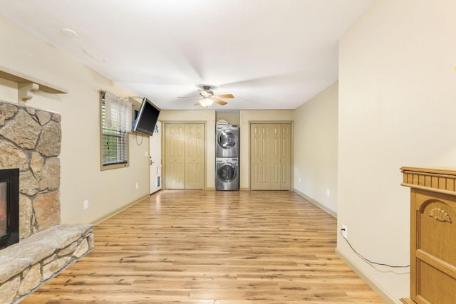 unfurnished living room with stacked washer / dryer, a stone fireplace, a ceiling fan, light wood-type flooring, and baseboards