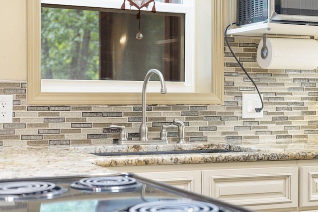 interior details featuring light stone counters, cream cabinetry, sink, and decorative backsplash