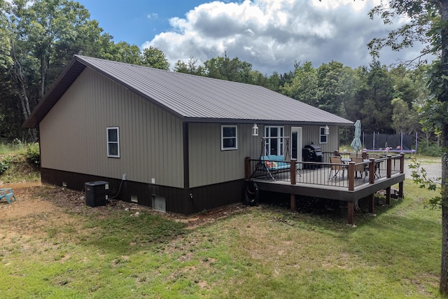 rear view of property featuring a yard, a wooden deck, central AC unit, and a trampoline