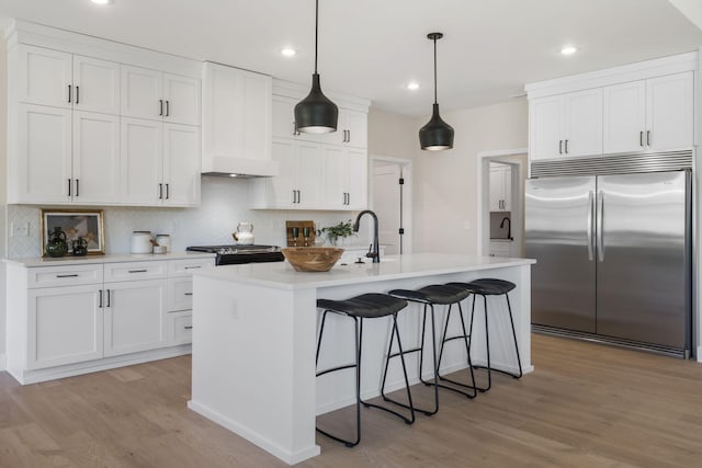 kitchen with white cabinetry, appliances with stainless steel finishes, decorative light fixtures, a kitchen island with sink, and light wood-type flooring