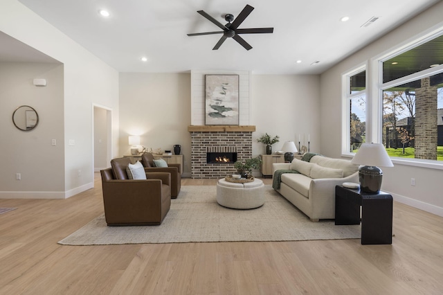 living room featuring a brick fireplace, light hardwood / wood-style floors, and ceiling fan