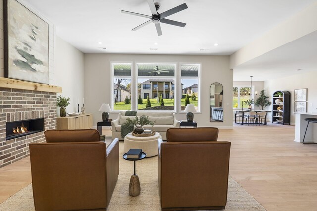 living room with ceiling fan, a wealth of natural light, a brick fireplace, and light hardwood / wood-style flooring