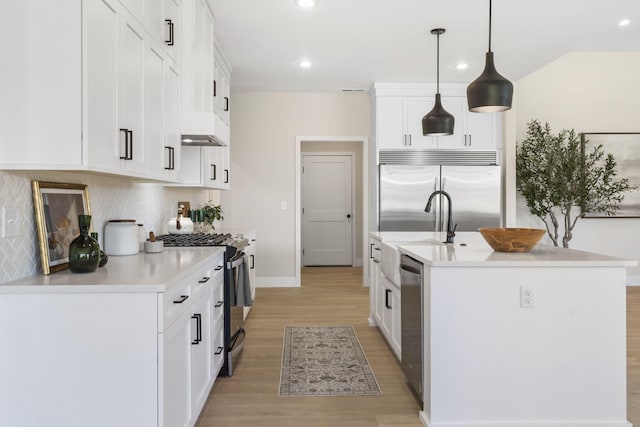 kitchen with a center island with sink, appliances with stainless steel finishes, decorative light fixtures, light hardwood / wood-style floors, and white cabinets