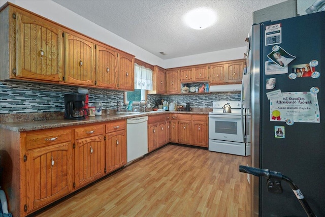 kitchen featuring tasteful backsplash, white appliances, light hardwood / wood-style flooring, sink, and a textured ceiling