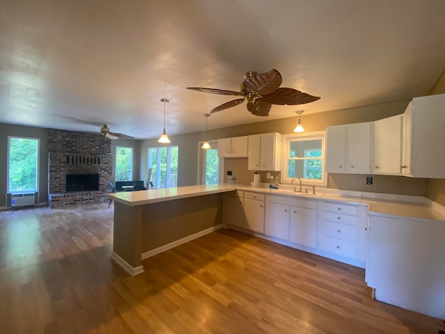 kitchen with white cabinets, pendant lighting, sink, wood-type flooring, and a fireplace