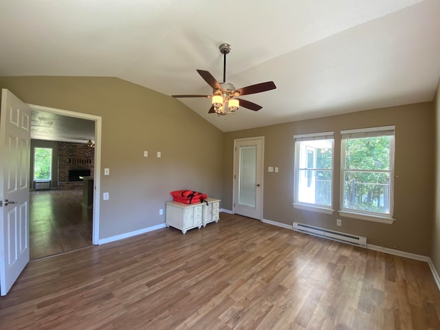 spare room with a brick fireplace, ceiling fan, lofted ceiling, a baseboard heating unit, and hardwood / wood-style flooring