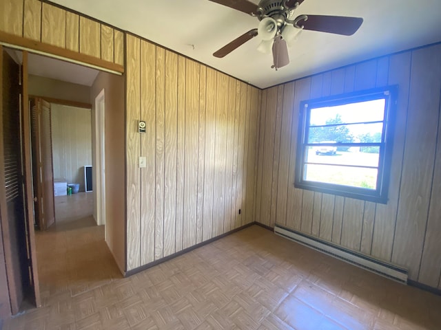 spare room featuring light parquet floors, a baseboard heating unit, wooden walls, and ceiling fan