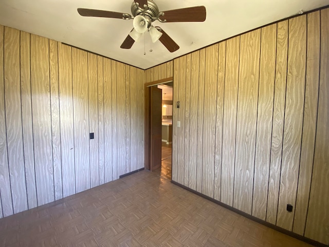 unfurnished bedroom with wood walls, dark parquet floors, and ceiling fan