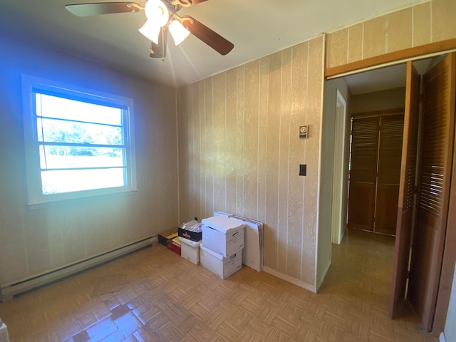 interior space featuring wood walls, baseboard heating, light parquet flooring, and ceiling fan