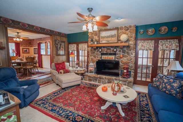 carpeted living room featuring ceiling fan, a stone fireplace, and french doors