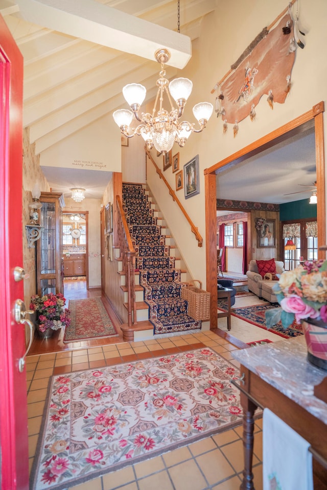 tiled entrance foyer featuring ceiling fan with notable chandelier, high vaulted ceiling, and beam ceiling