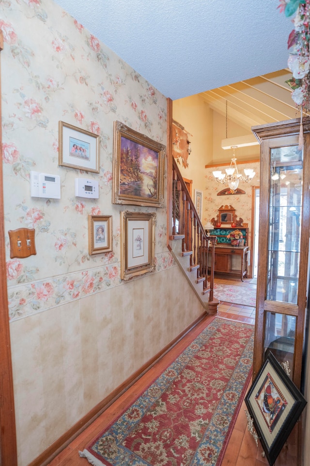 hall featuring a textured ceiling, hardwood / wood-style floors, a chandelier, and vaulted ceiling