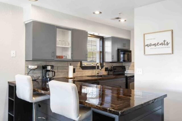 kitchen featuring gray cabinetry, kitchen peninsula, decorative backsplash, and black appliances