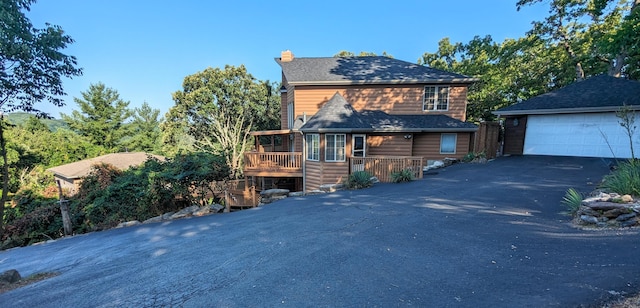 view of front facade featuring a chimney, faux log siding, a deck, and a detached garage