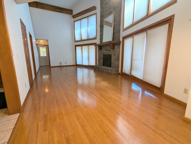 unfurnished living room featuring light wood finished floors, a towering ceiling, beamed ceiling, baseboards, and a fireplace