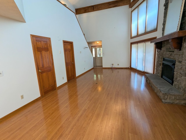 unfurnished living room with high vaulted ceiling, beam ceiling, a stone fireplace, and light hardwood / wood-style floors