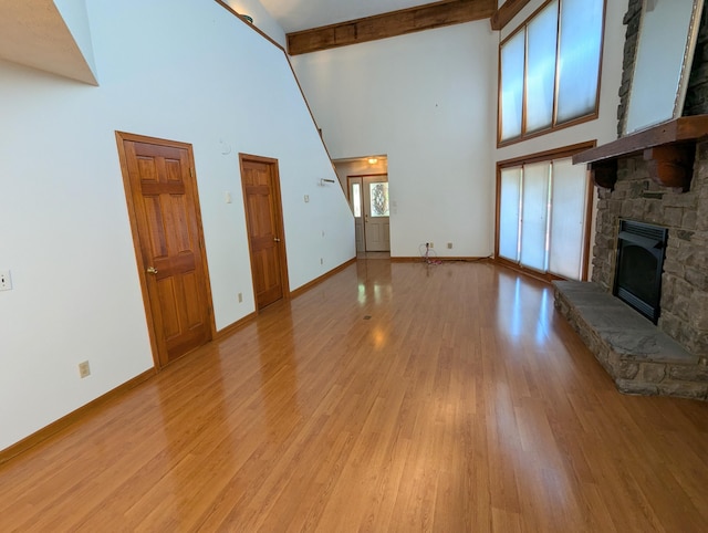 unfurnished living room featuring beam ceiling, baseboards, light wood-style floors, a stone fireplace, and high vaulted ceiling