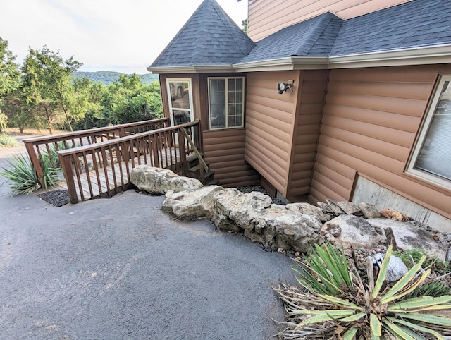 view of exterior entry with a wooden deck, roof with shingles, and log veneer siding