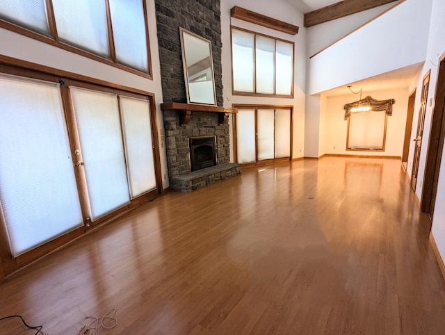 unfurnished living room with beam ceiling, a chandelier, high vaulted ceiling, hardwood / wood-style flooring, and a fireplace