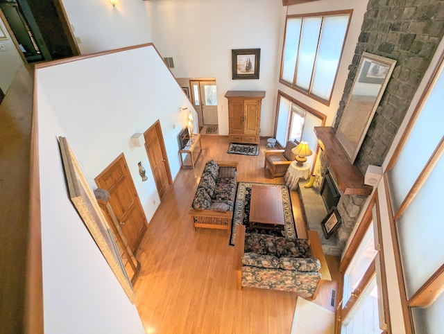 living room with a high ceiling, light wood-type flooring, and a stone fireplace