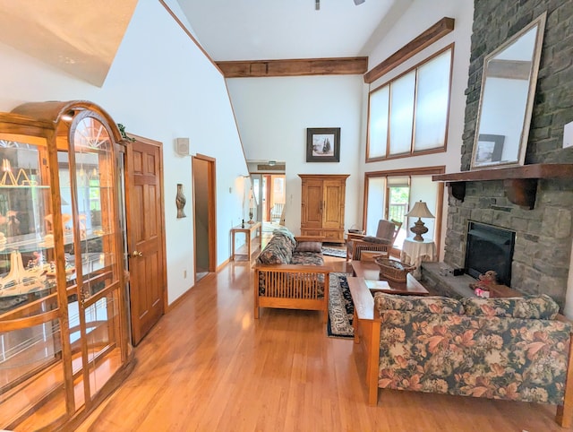 living room with light hardwood / wood-style floors, high vaulted ceiling, beam ceiling, and a stone fireplace