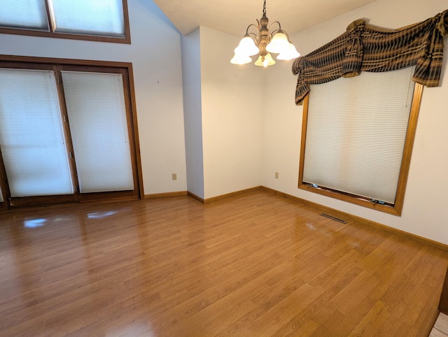 empty room with baseboards, wood finished floors, a chandelier, and visible vents