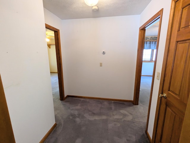 hallway with dark colored carpet, baseboards, and a textured ceiling