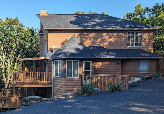 exterior space featuring a shingled roof, faux log siding, and a deck
