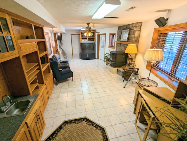 living area featuring light tile patterned floors, a ceiling fan, visible vents, and a wood stove